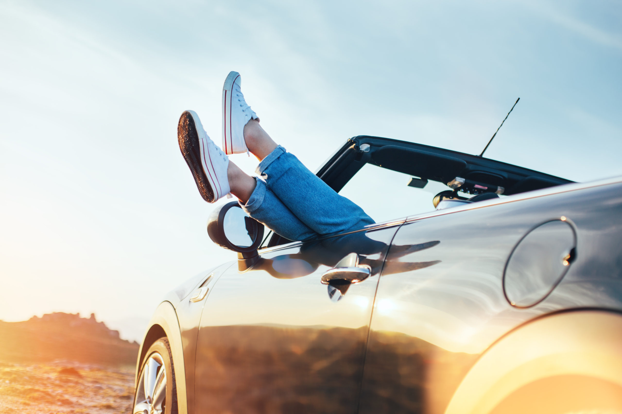 A young woman rests her legs out the passenger door of a convertible. Car and personal Loans