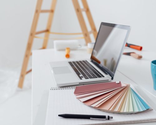 Home makeover, renovation and decoration: laptop on a desktop with color swatches and paint rollers. A small personal loan was required to complete the renovations.